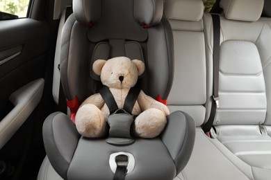 Photo of Teddy bear fastened with car safety belt in child seat