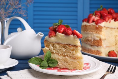 Piece of tasty cake with fresh strawberries, mint and cup of tea on table