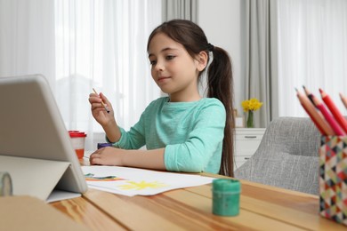 Little girl drawing on paper with paints at online lesson indoors. Distance learning