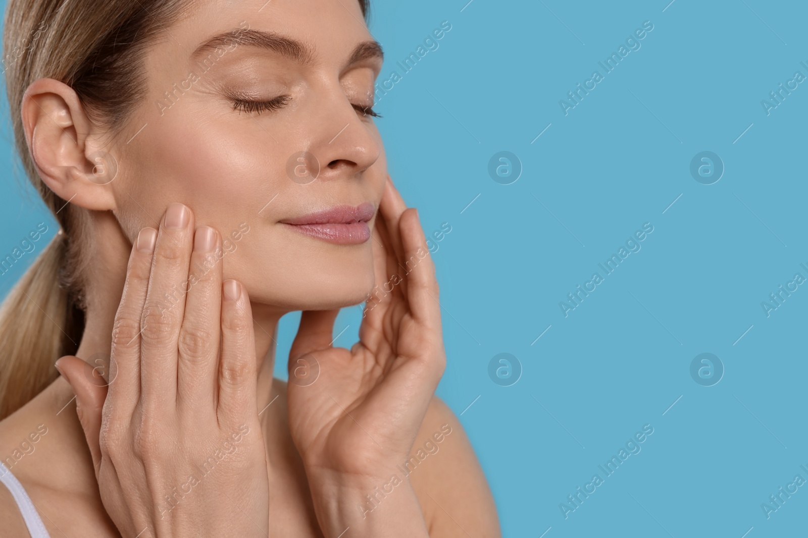 Photo of Woman massaging her face on turquoise background. Space for text