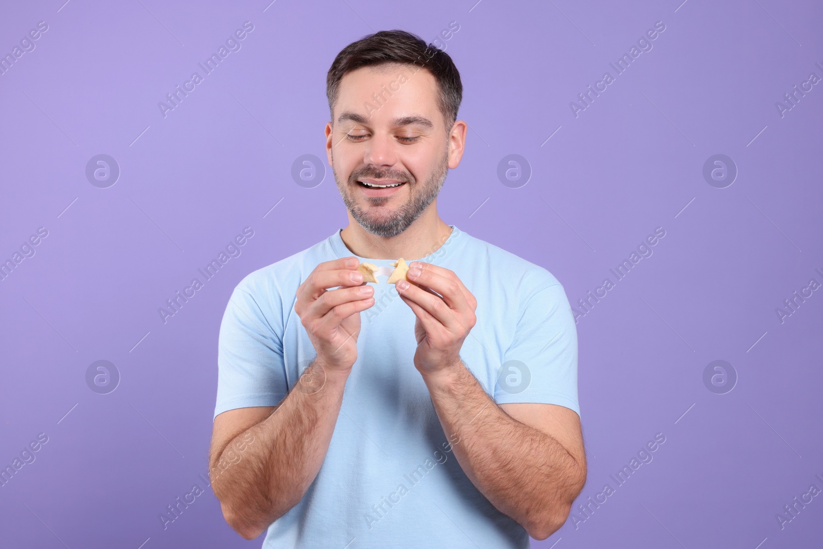 Photo of Happy man holding tasty fortune cookie with prediction on violet background