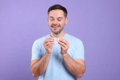 Photo of Happy man holding tasty fortune cookie with prediction on violet background