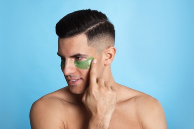 Photo of Man applying green under eye patch on light blue background