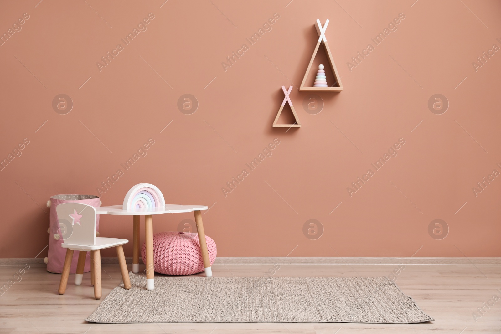 Photo of Cute child room interior with furniture, toys and wigwam shaped shelves on pink wall