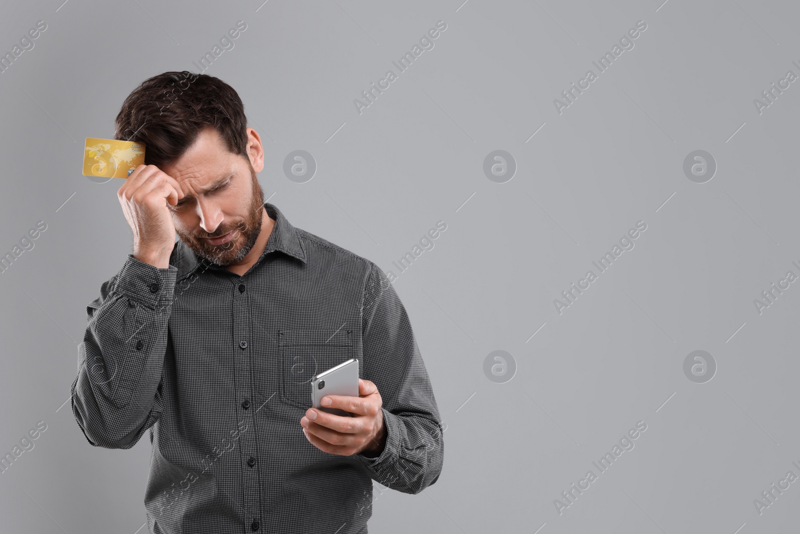 Photo of Upset man with smartphone and credit card on light grey background, space for text. Be careful - fraud