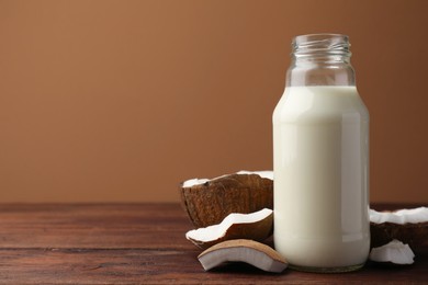 Bottle of delicious vegan milk and coconut pieces on wooden table, space for text