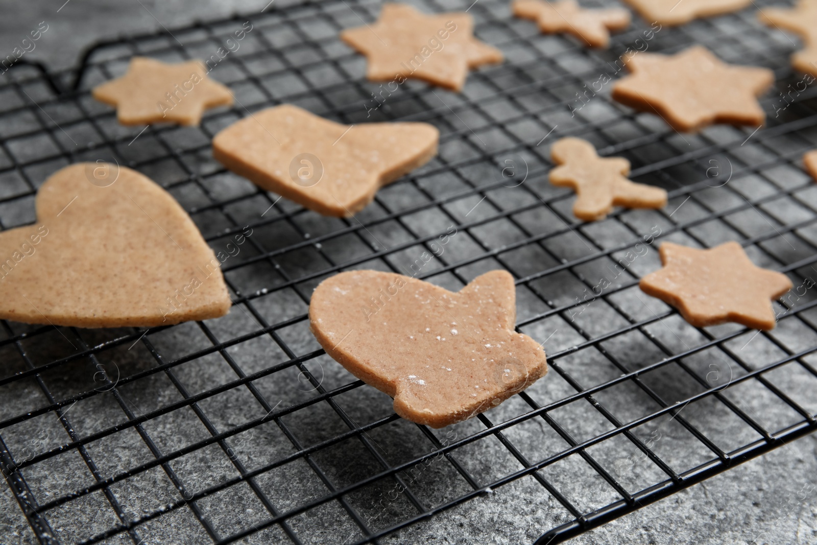 Photo of Homemade Christmas cookies. Baking rack with raw gingerbread biscuits on grey table, closeup