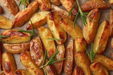 Tasty baked potato and aromatic rosemary on parchment paper, flat lay