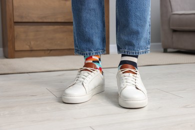 Photo of Man in different stylish socks, sneakers and jeans indoors, closeup