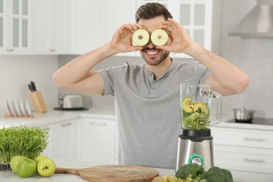Photo of Man covering eyes with halves of apples in kitchen. Making smoothie