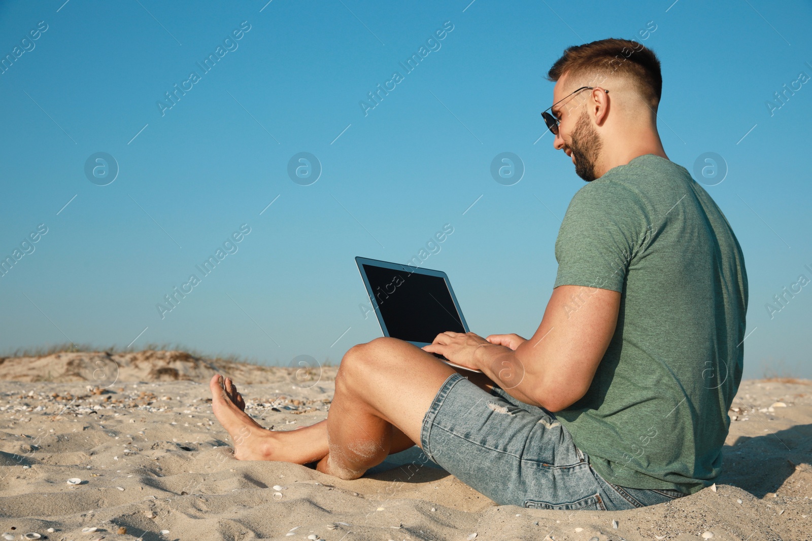 Photo of Man working with modern laptop on beach