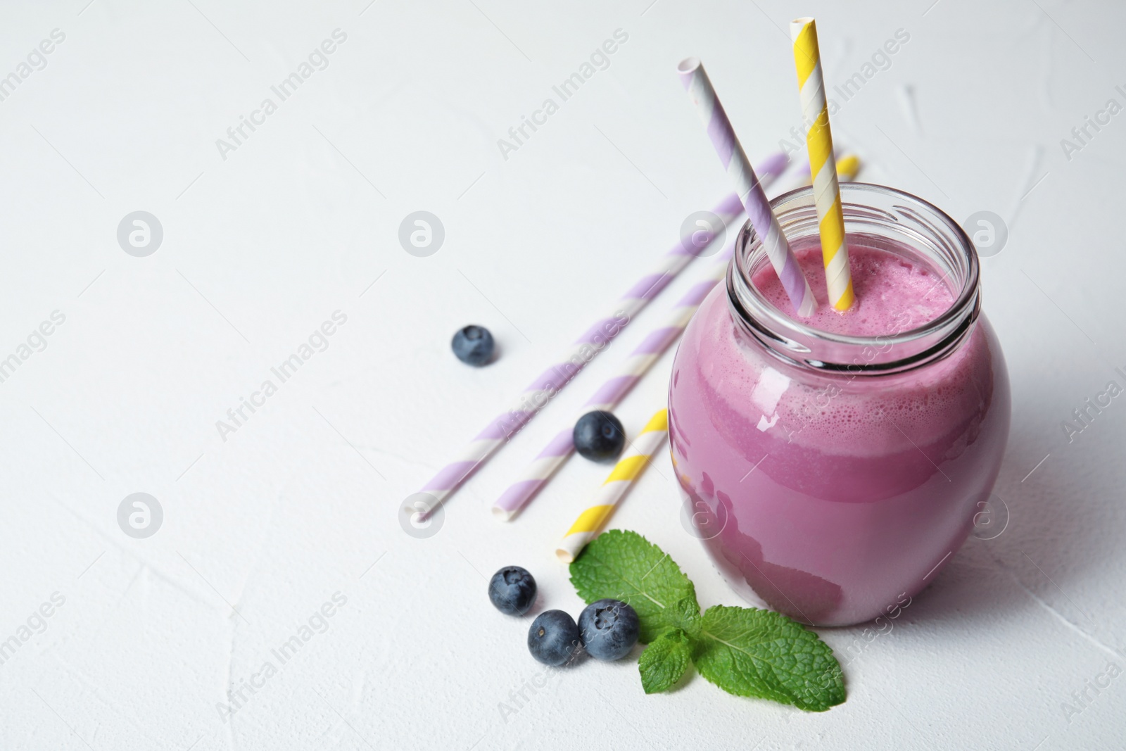 Photo of Jar of tasty milk shake and blueberries on light background. Space for text