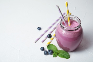 Photo of Jar of tasty milk shake and blueberries on light background. Space for text
