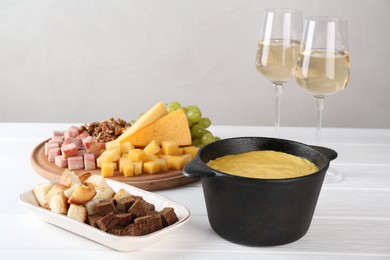 Photo of Fondue with tasty melted cheese, different products and aromatic wine in glasses on white wooden table