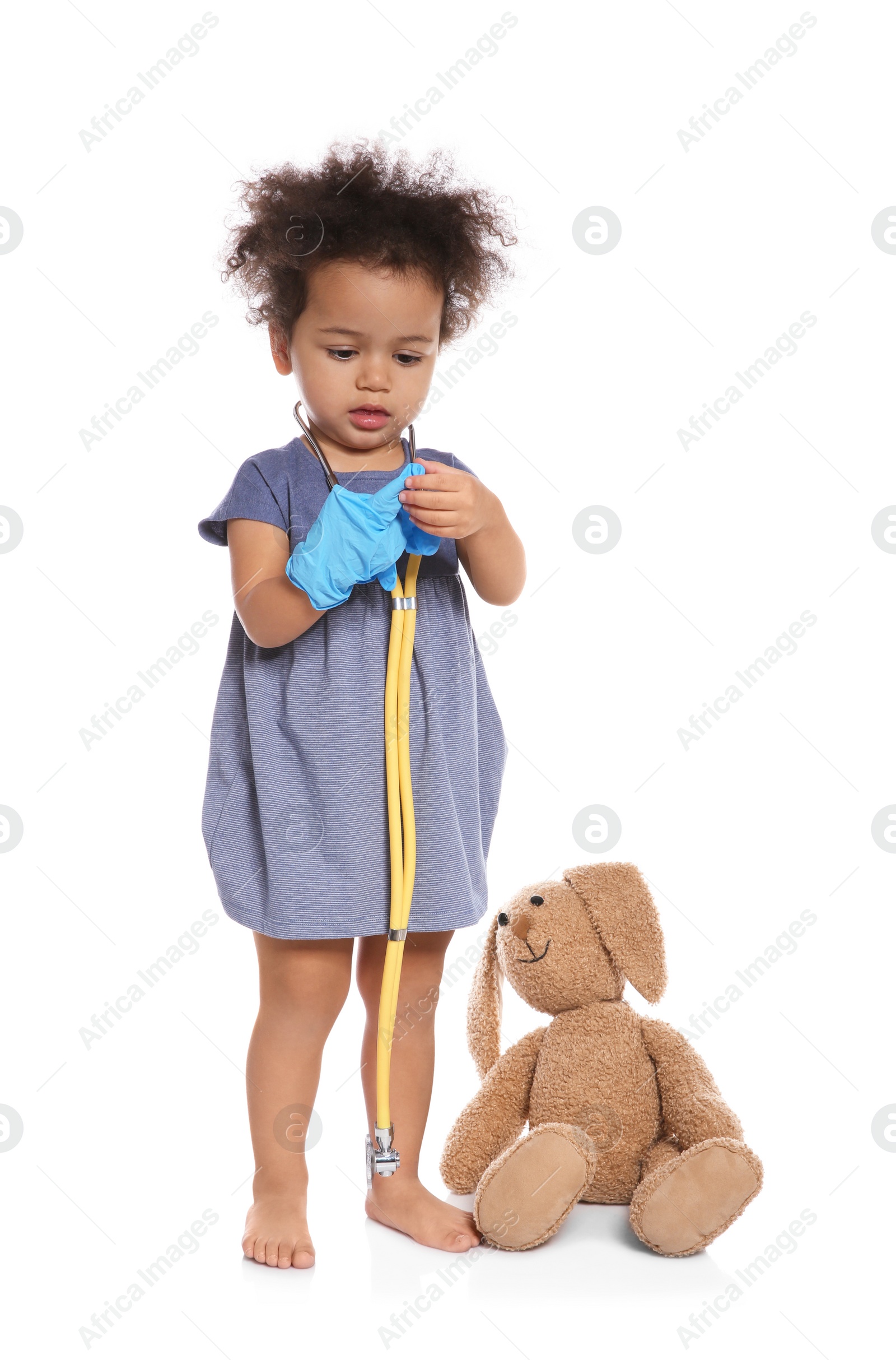 Photo of Cute African American child imagining herself as doctor while playing with stethoscope and toy bunny on white background