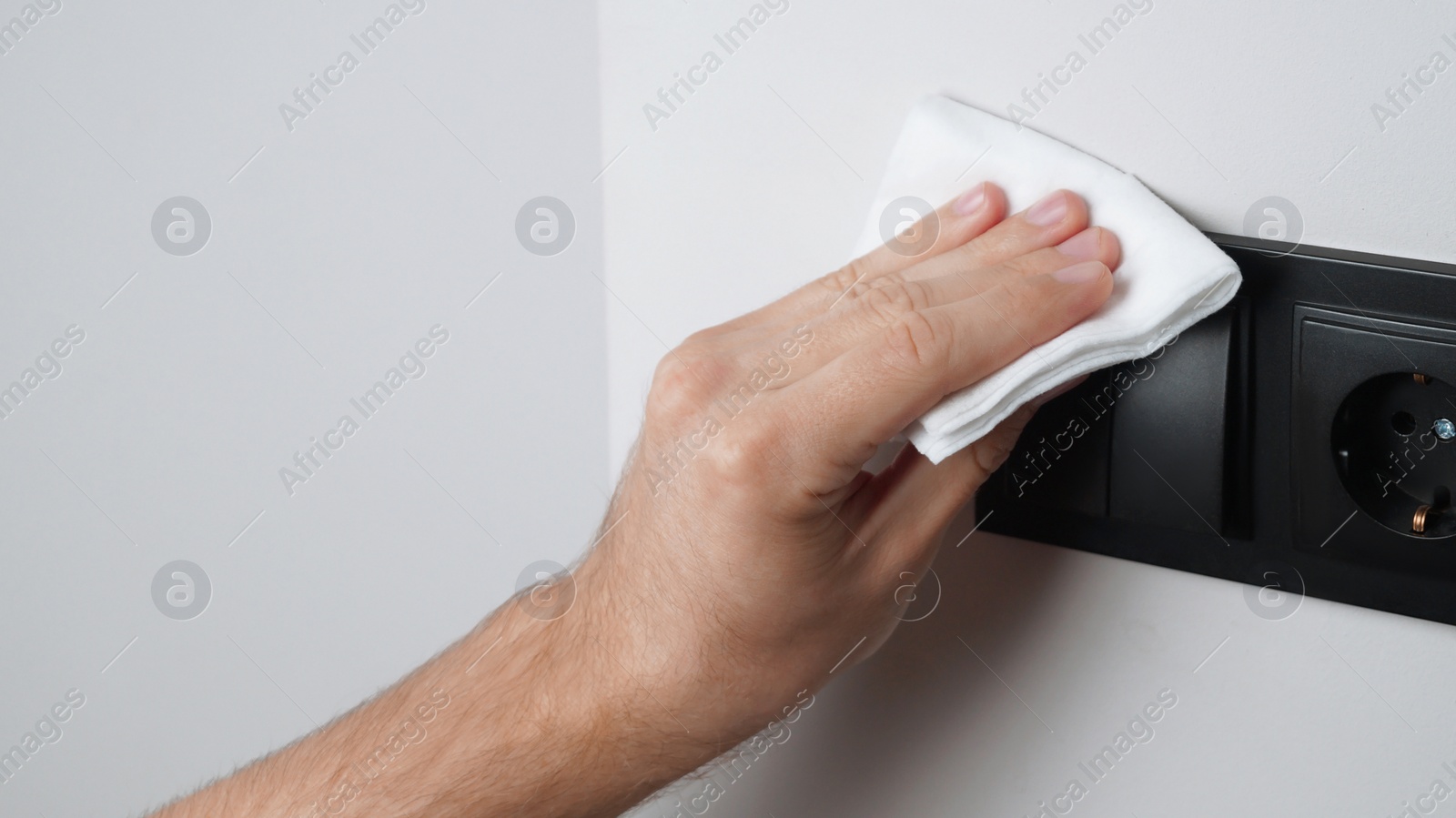 Photo of Man cleaning light switch with wet wipe indoors, closeup. Protective measures