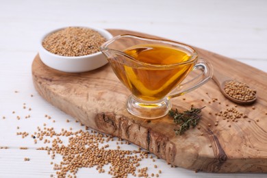 Photo of Jug of natural oil and mustard seeds on white wooden table