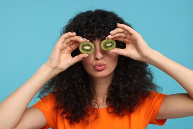 Photo of Woman covering eyes with halves of kiwi on light blue background