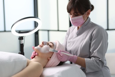 Photo of Cosmetologist applying mask on woman's face in clinic