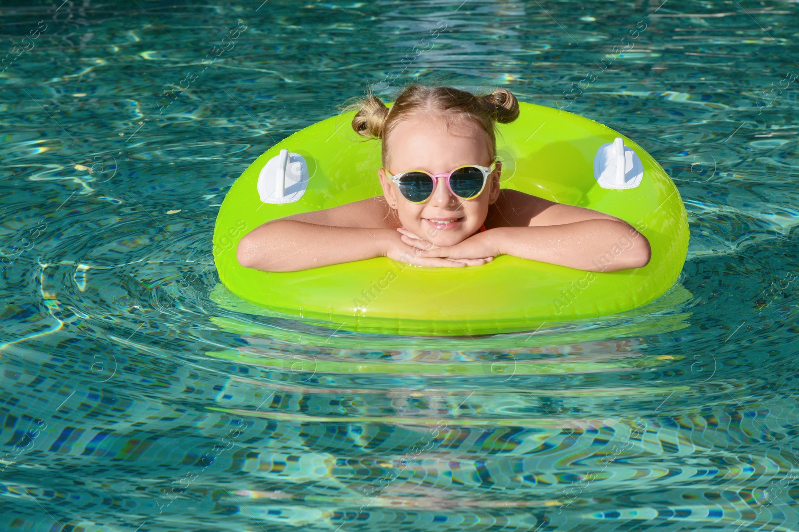 Photo of Happy little girl with inflatable ring in outdoor swimming pool on sunny day