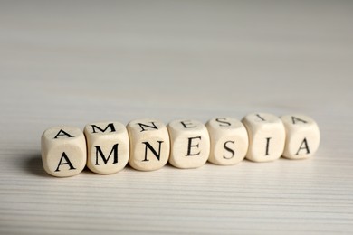 Cubes with word Amnesia on white wooden table, closeup view