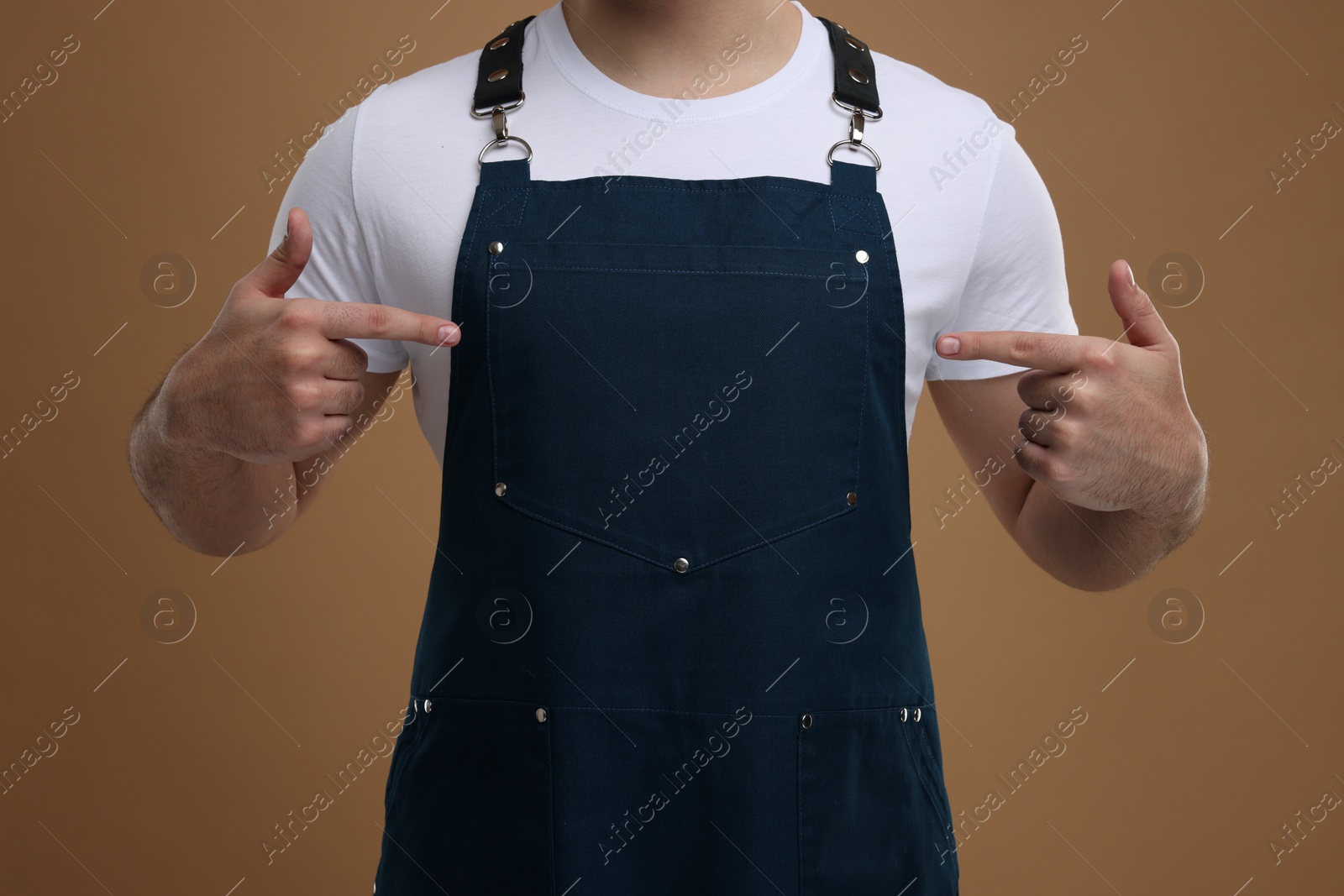 Photo of Man pointing at kitchen apron on brown background, closeup. Mockup for design