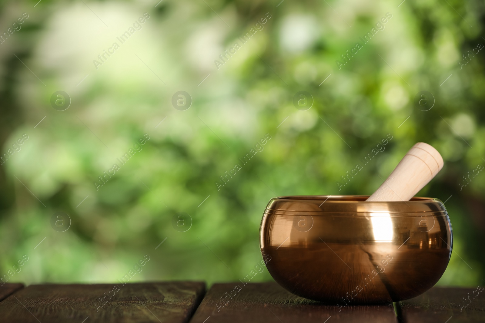 Photo of Golden singing bowl with mallet on wooden table outdoors, space for text