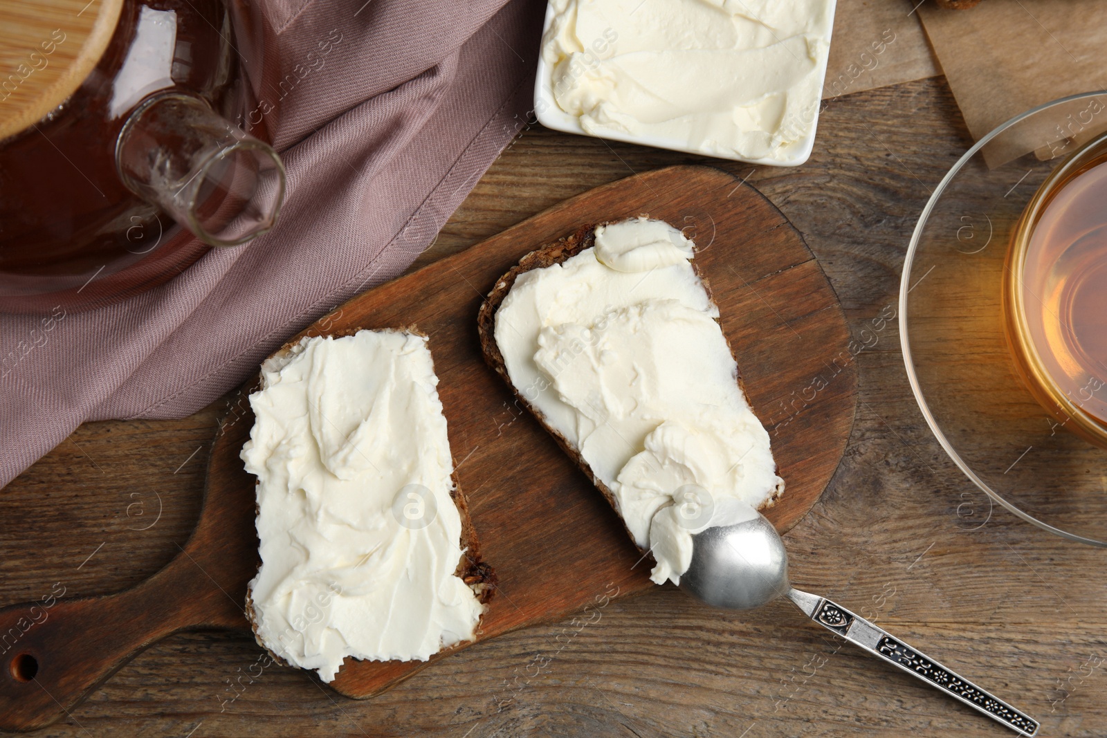 Photo of Bread with cream cheese on wooden table, flat lay
