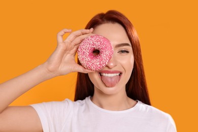 Happy woman with red dyed hair and donut on orange background