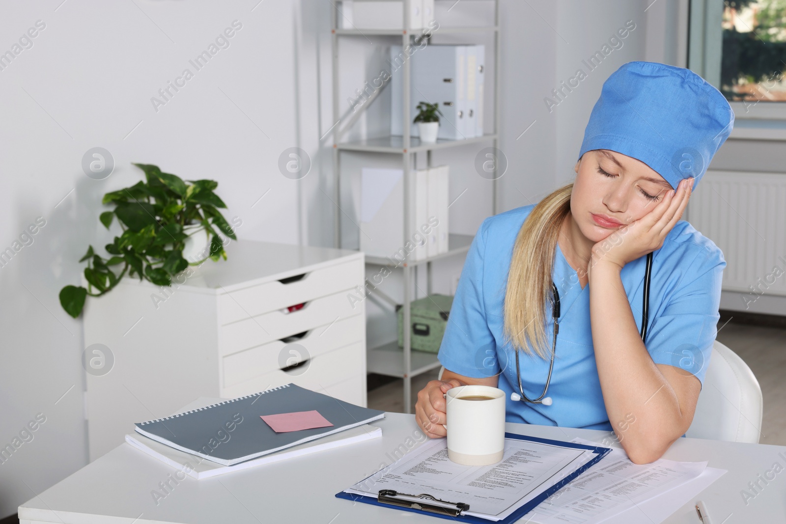 Photo of Tired young doctor sleeping at workplace in office