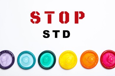 Colorful condoms and text STOP STD on white background, flat lay