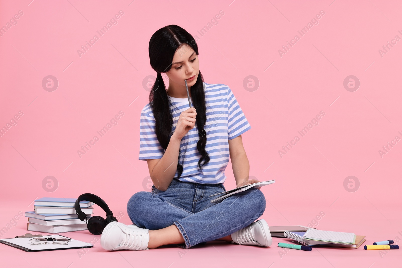 Photo of Student with notebook sitting among books and stationery on pink background