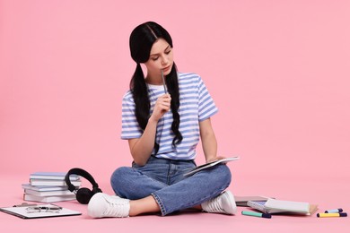 Student with notebook sitting among books and stationery on pink background