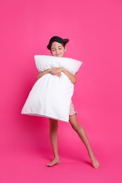 Photo of Cute girl in pajamas hugging pillow on pink background