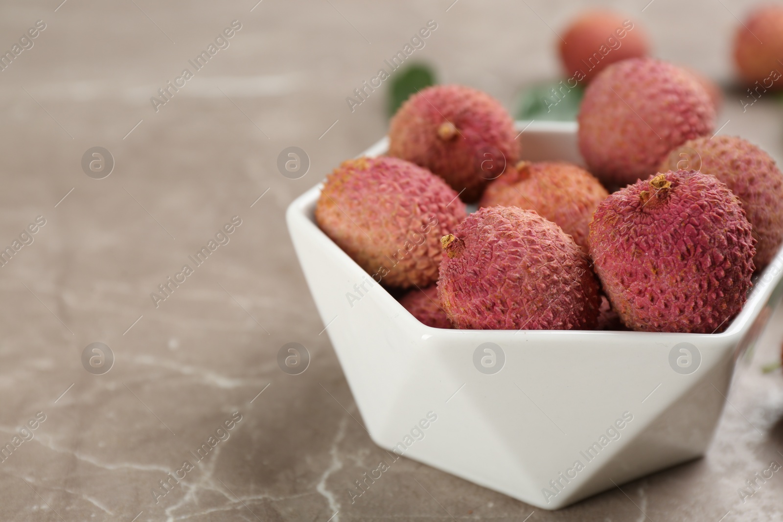 Photo of Fresh ripe lychee fruits in ceramic bowl on grey table. Space for text