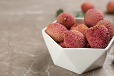 Fresh ripe lychee fruits in ceramic bowl on grey table. Space for text