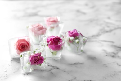 Photo of Ice cubes with roses on marble background, space for text