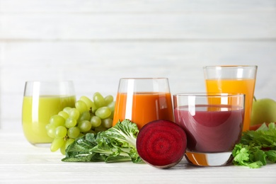 Glasses with different juices and fresh ingredients on table