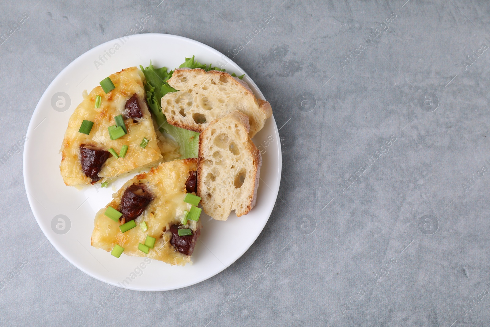 Photo of Tasty sausage casserole with green onion and bread on grey table, top view. Space for text