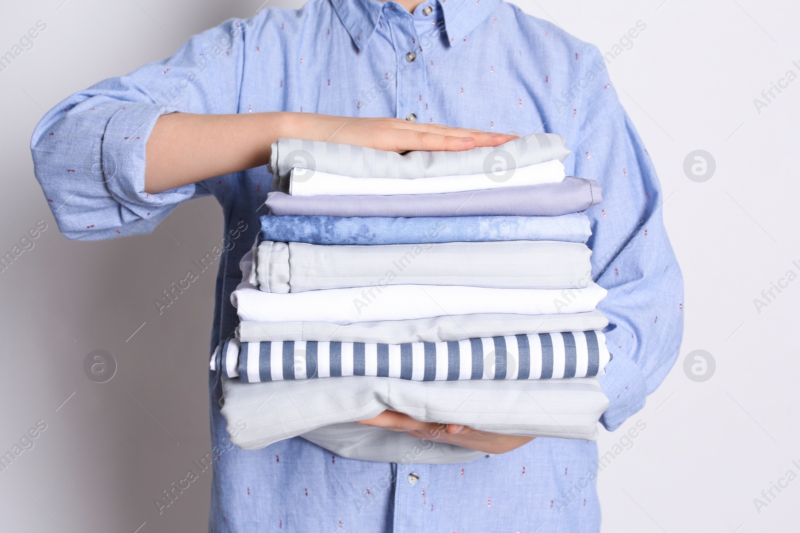 Photo of Woman holding stack of clean bed linens on white background, closeup