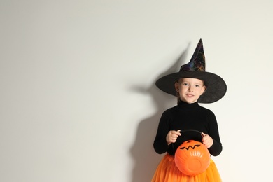 Photo of Cute little girl with pumpkin candy bucket wearing Halloween costume on light background. Space for text