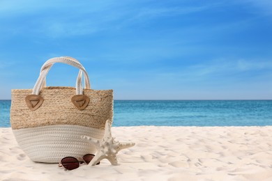 Image of Bag with sunglasses and starfish on sunny ocean beach, space for text. Summer vacation