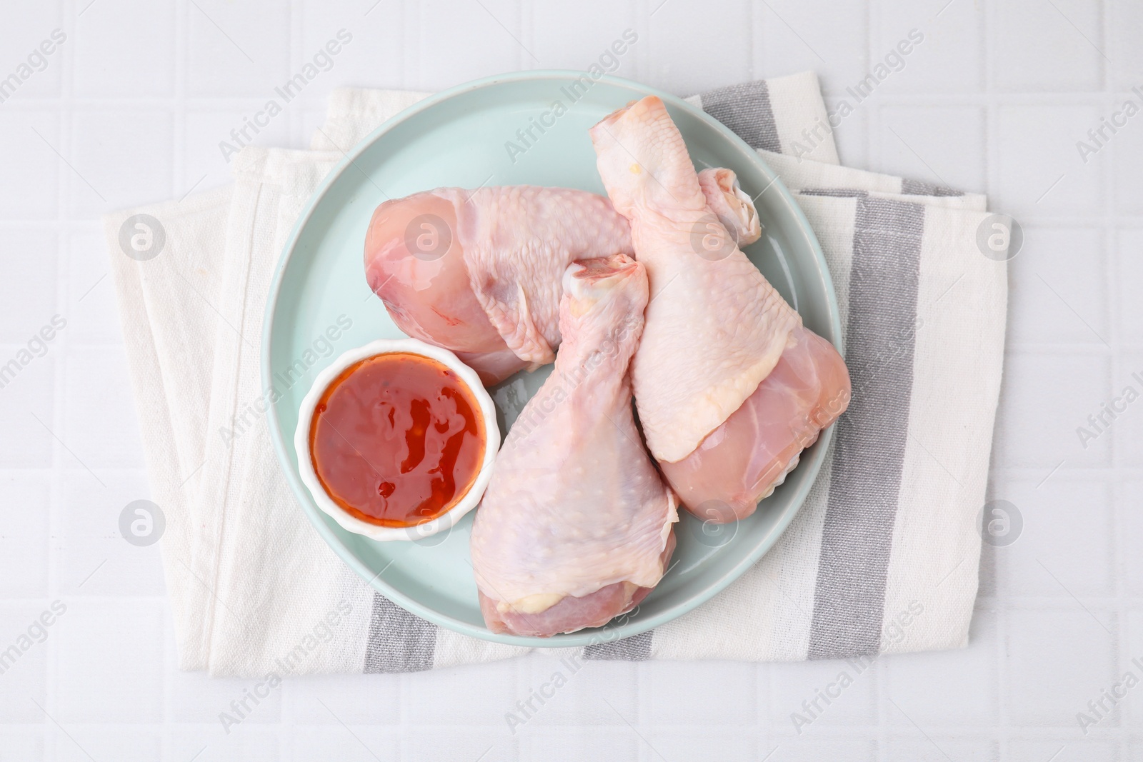 Photo of Fresh marinade and raw chicken drumsticks on white tiled table, top view