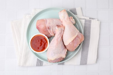Fresh marinade and raw chicken drumsticks on white tiled table, top view