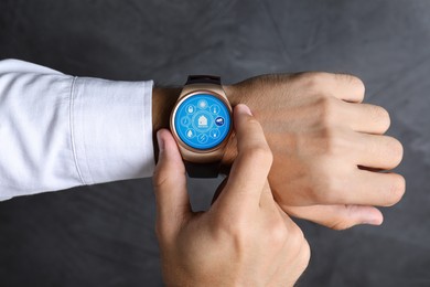 Image of Man setting smart home control system via smartwatch against dark grey background, closeup. App interface with icons on display