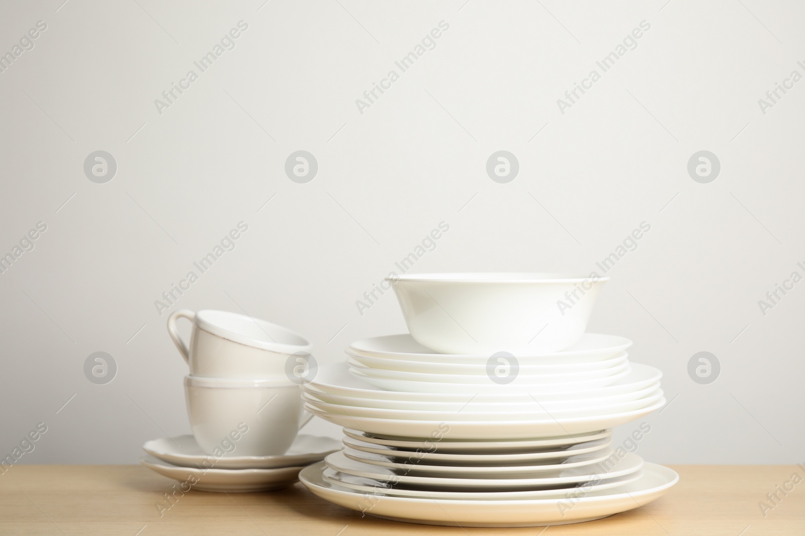 Photo of Clean plates, bowl and cups on wooden table against white background. Space for text