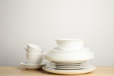 Photo of Clean plates, bowl and cups on wooden table against white background. Space for text