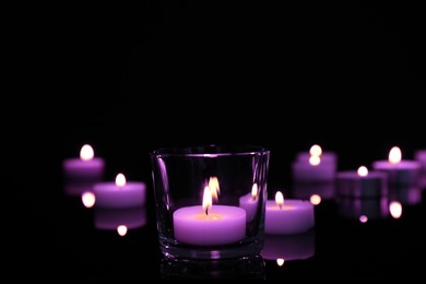 Image of Burning violet candle on black background, closeup. Funeral attributes