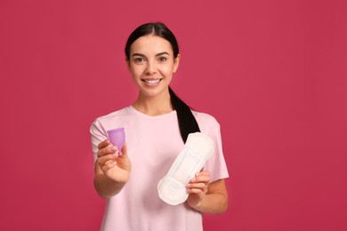 Photo of Young woman with menstrual cup and pad on bright pink background