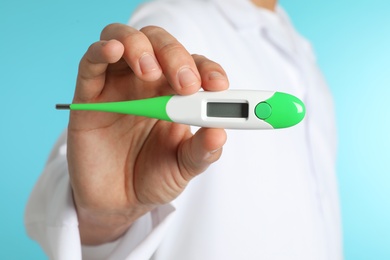 Male doctor holding digital thermometer on color background, closeup. Medical object